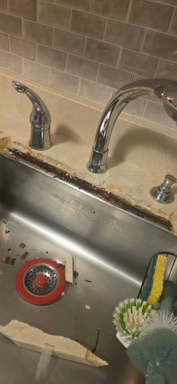 Severely broken Crema Marfil marble edge around a stainless-steel sink