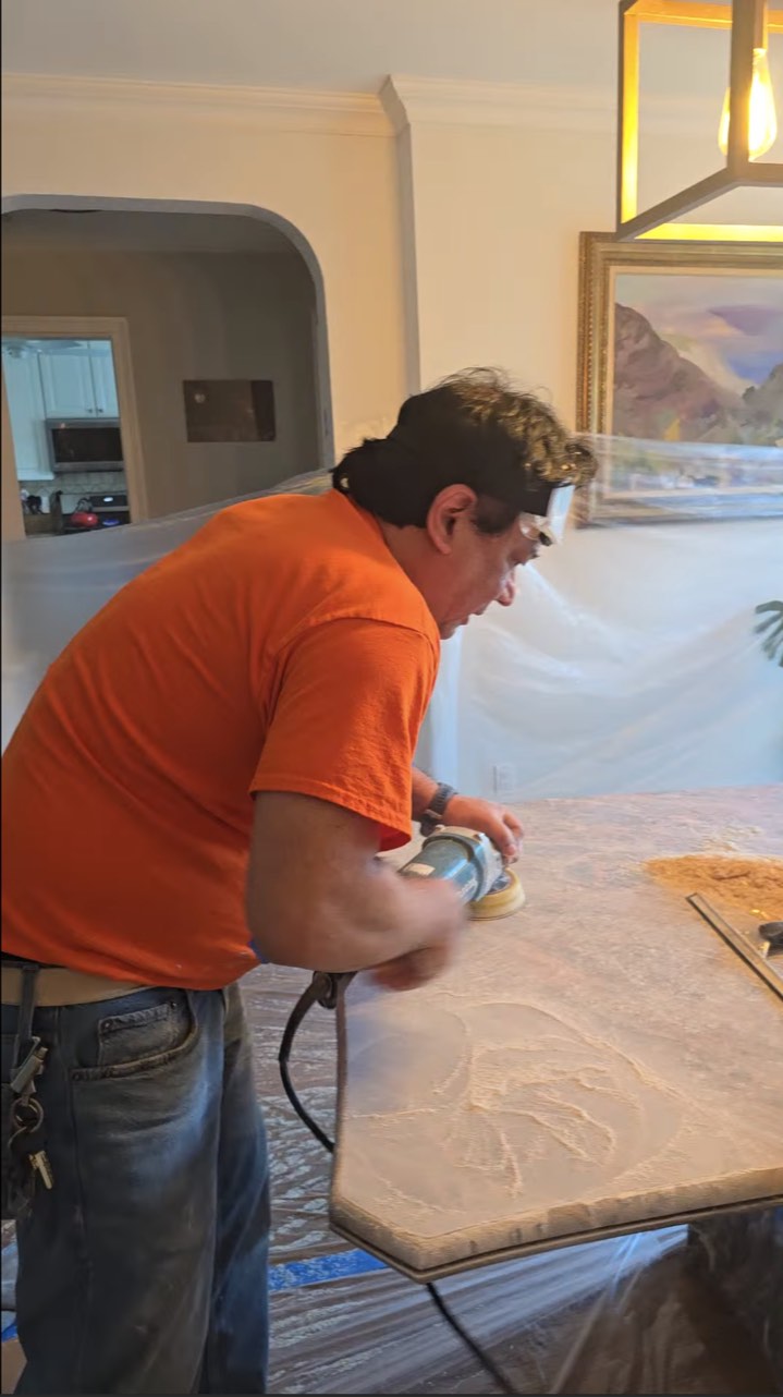 Technician honing a stone dining table with a handheld machine in a protected apartment